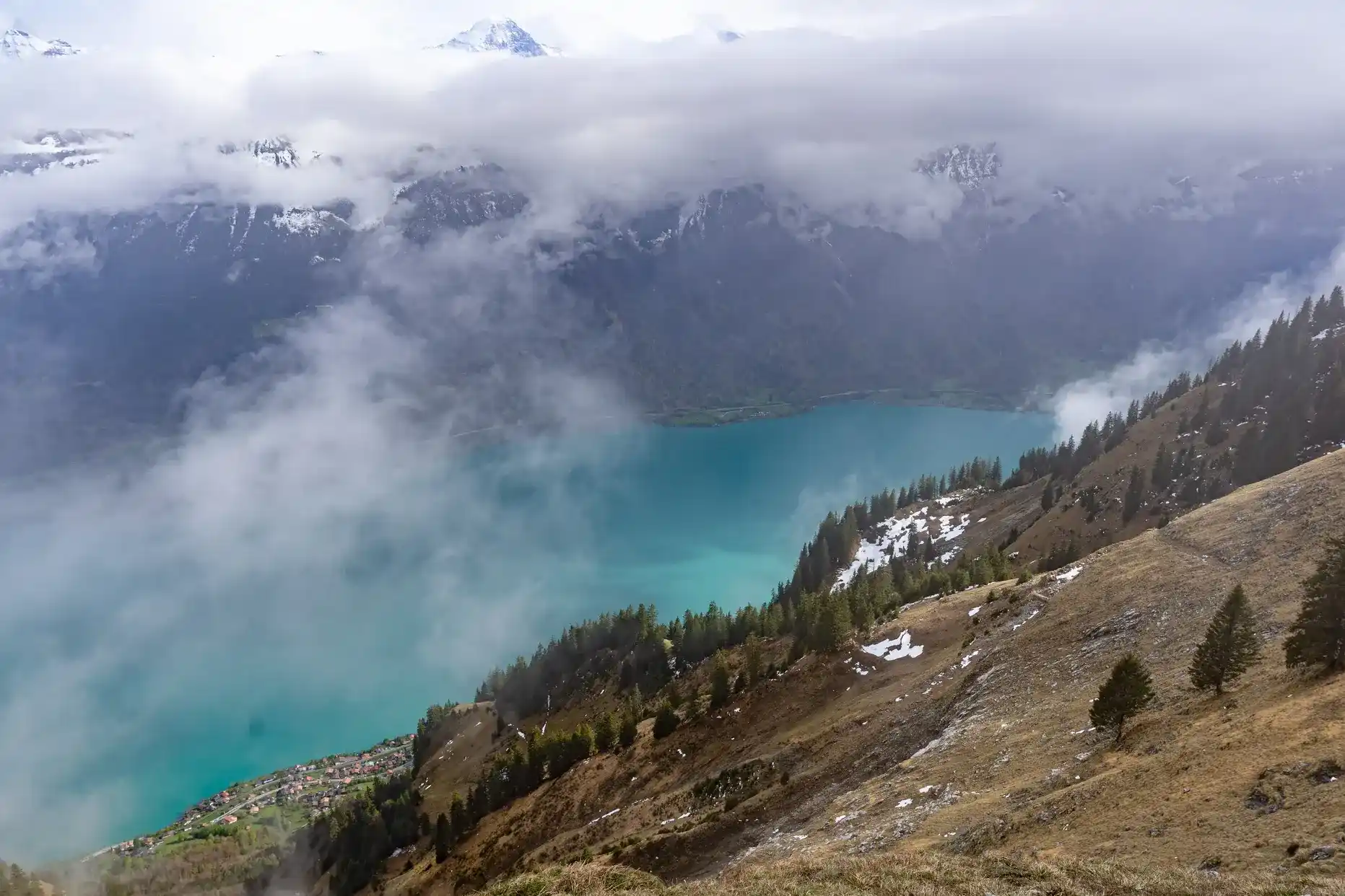 Lac turquoise au pied de montagnes enneigées dans la brume