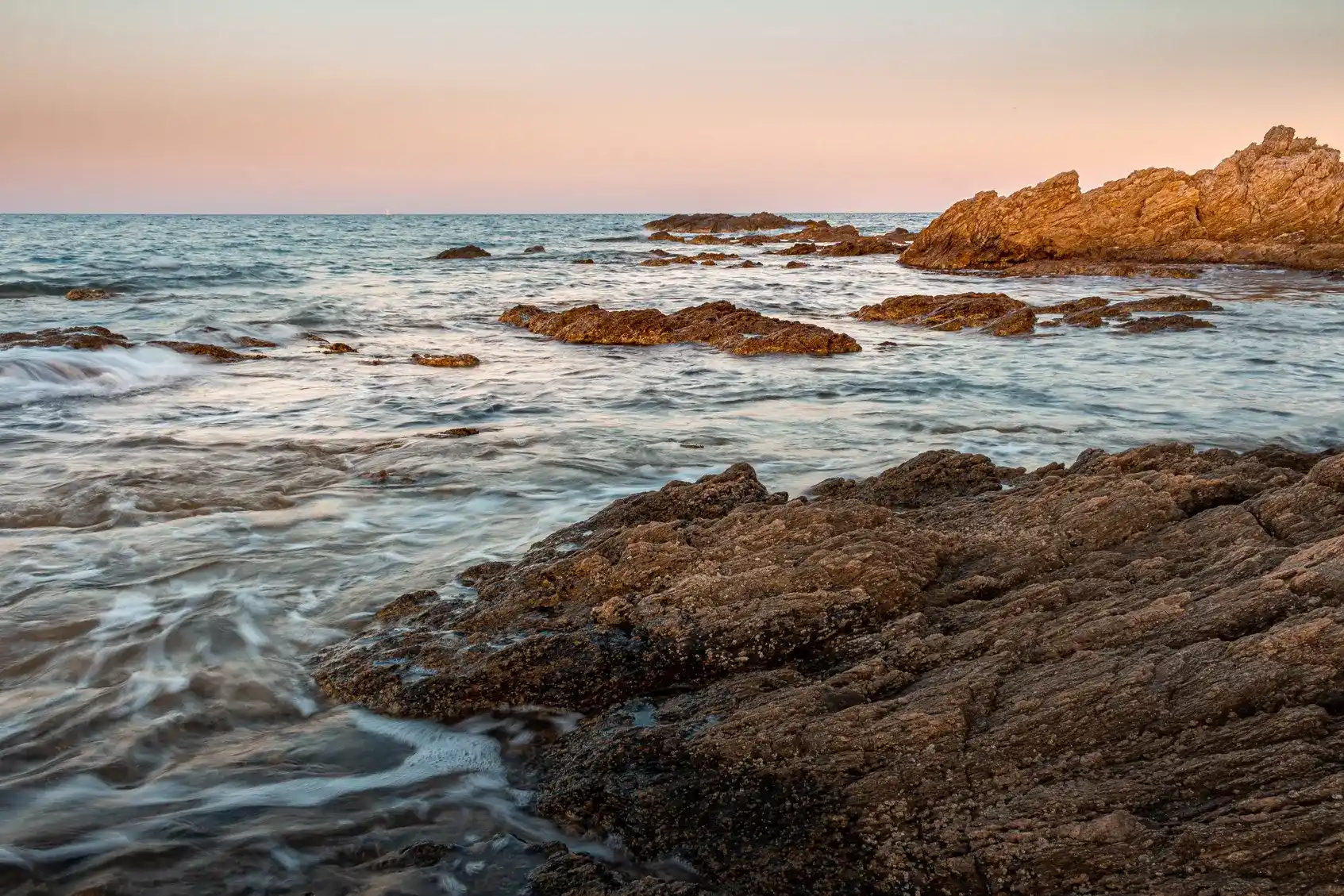 Vagues sur une côte rocheuse sous un ciel rosé